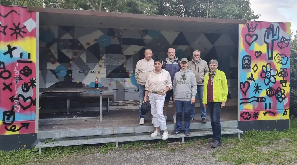 Gruppenfoto vor einem Container mit Bank und Tisch, an der Wand Grafitti