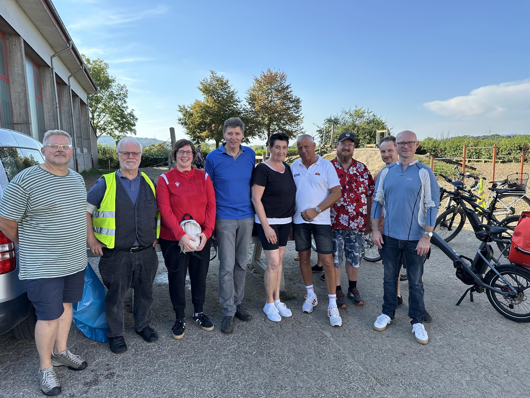 Gruppenbild auf Parkplatz, mit Fahrrädern, Bäumen und Wiehengebierge im Hintergrund