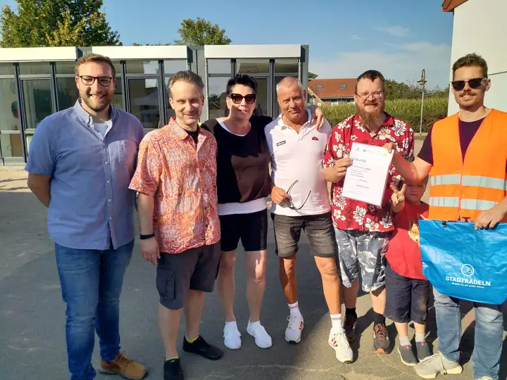 Gruppenbild in der Stadt im Sonnenschein, Maik Biermann präsentiert Urkunde