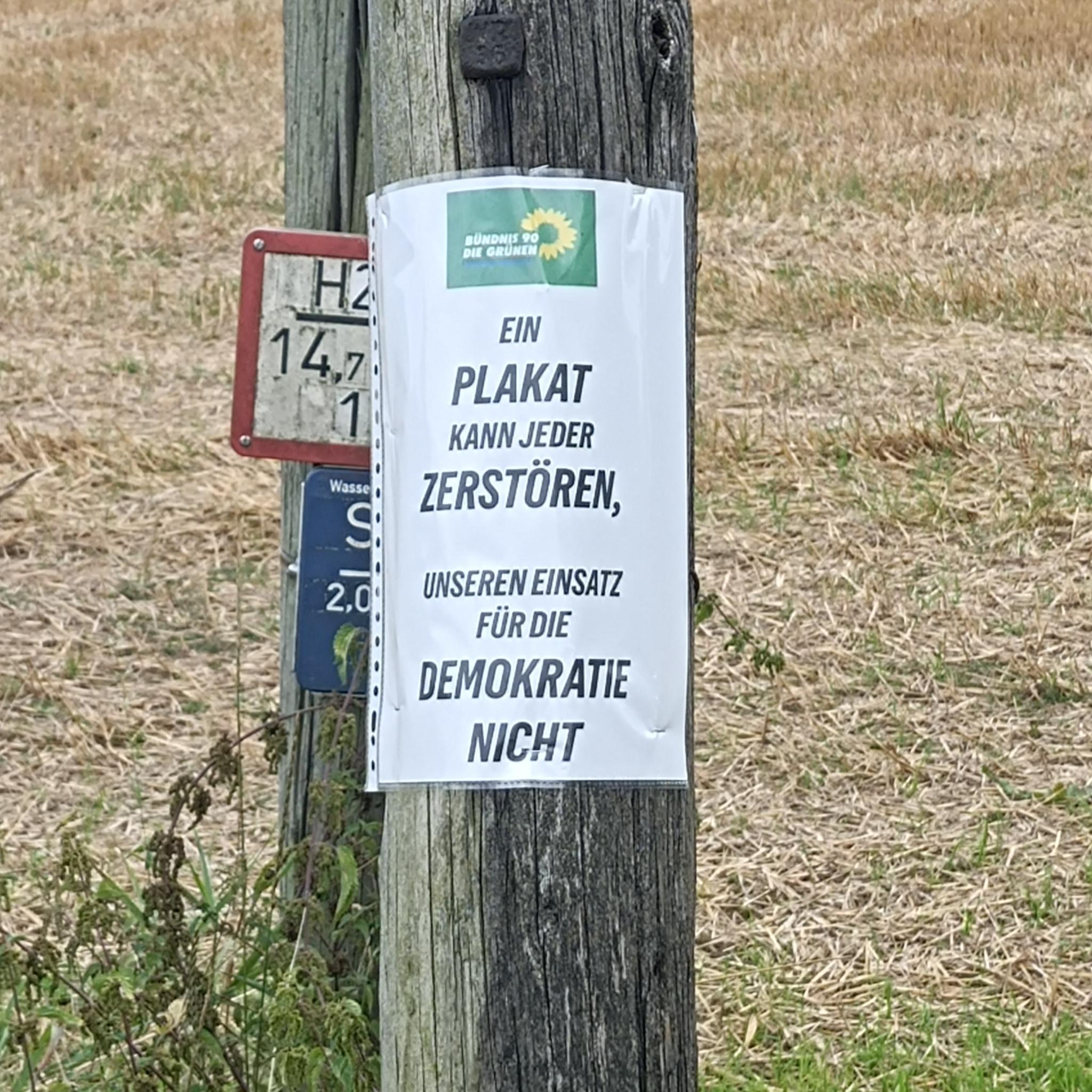 Zettel am Mast mit grünem Logo "Ein Plakat kann jeder zerstören, unseren Einsatz für die Demokratie nicht"
